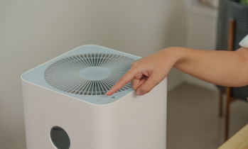 A person’s hand presses the power button on a white air purifier.